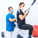 Physiotherapist in blue gown and a patient with rubber arm exercises