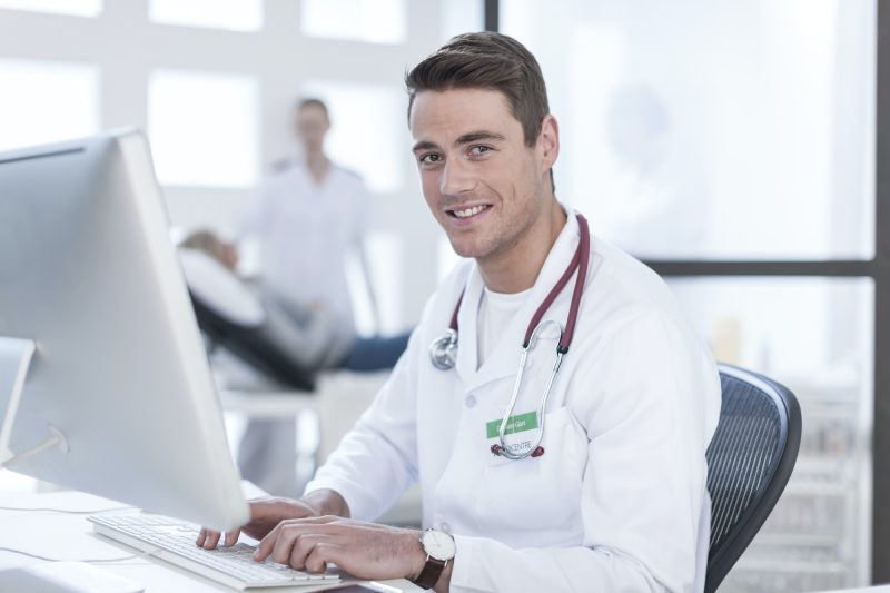 Portrait of smiling doctor sitting at desk working on computer